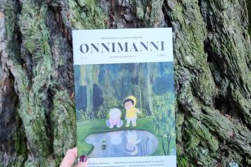 Onnimanni-lehden numero 3/25 puunrunkoa vasten.