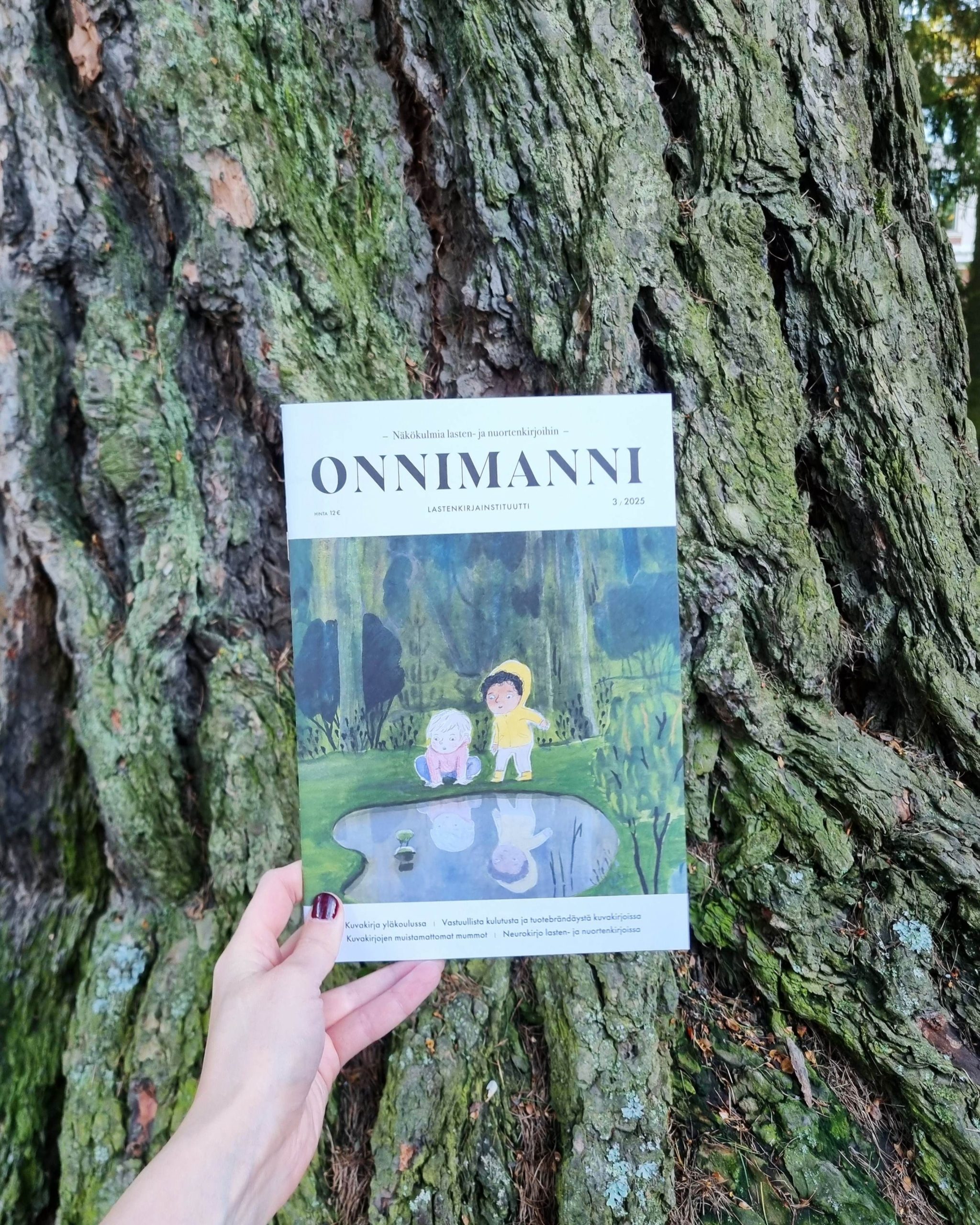 Onnimanni-lehden numero 3/25 puunrunkoa vasten.