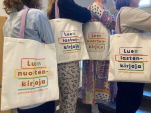 Ihmisiä, joilla on olalla Luen lastenkirjoja ja Luen nuortenkirjoja -kangaskassit.