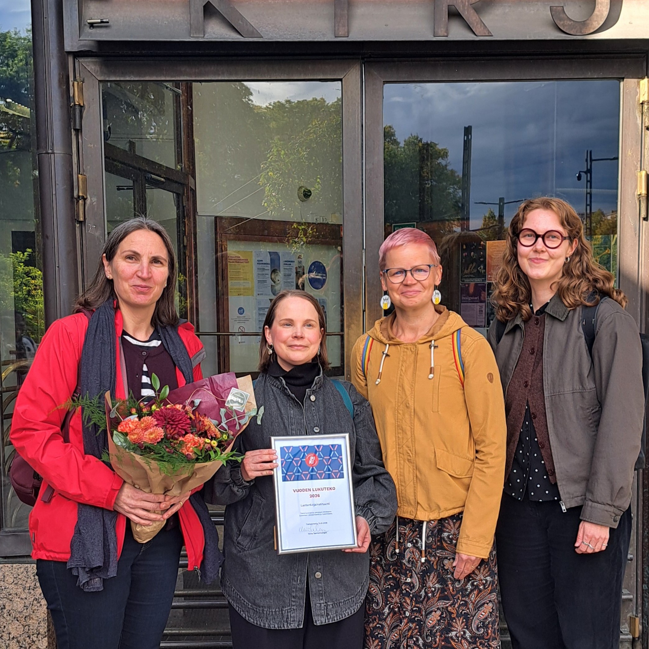 Lastenkirjainstituutin henkilökunta seisomassa Tampereen pääkirjasto Metson ovien edessä.
